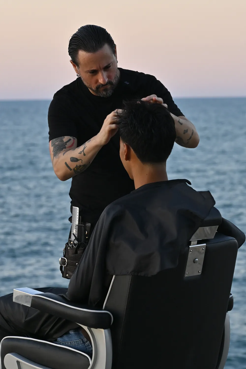 Matteo Soccio sistema i capelli di un cliente sulla scogliera di Termoli, con il mare alle spalle