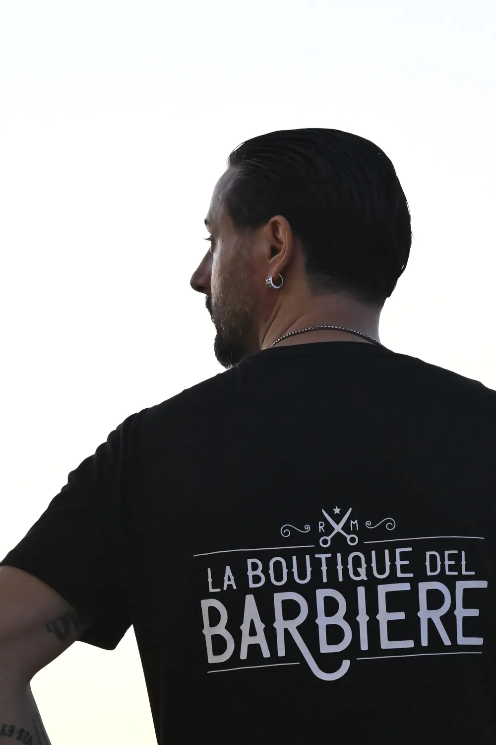Matteo di spalle con la maglia La Boutique del Barbiere, davanti al mare al tramonto